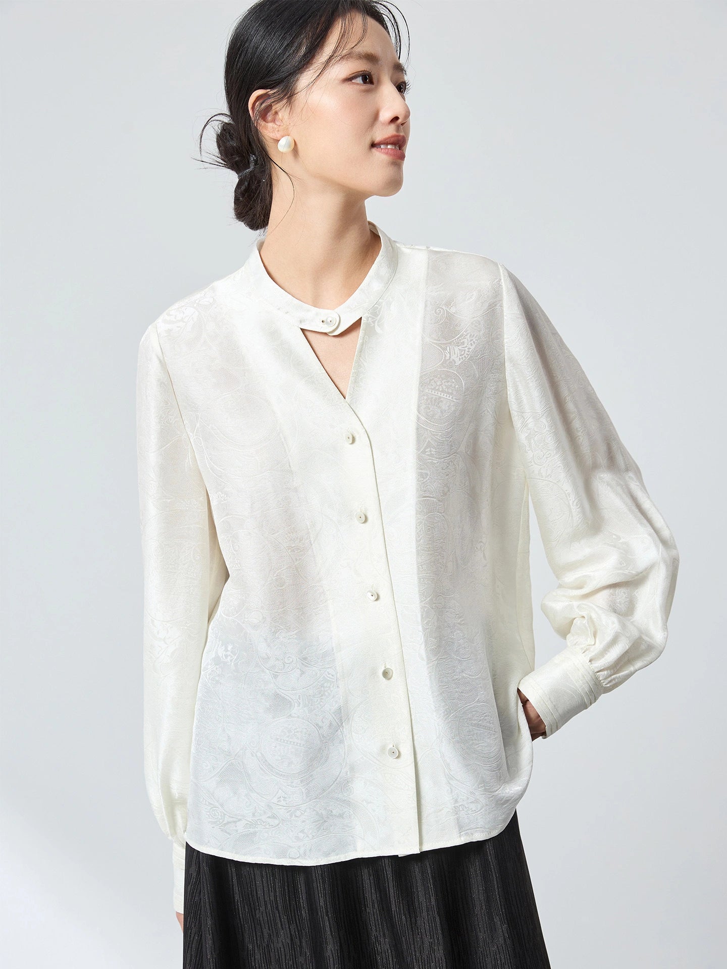 Model wearing a white long-sleeve jacquard blouse with a stand collar, featuring a relaxed fit and subtle floral pattern, perfect for a refined New Chinese look.