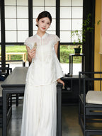 Model wearing a white lace-trimmed Cheongsam top with a mandarin collar and floral embroidery, holding a fan, crafted from 80% Viscose, 20% Polyamide.