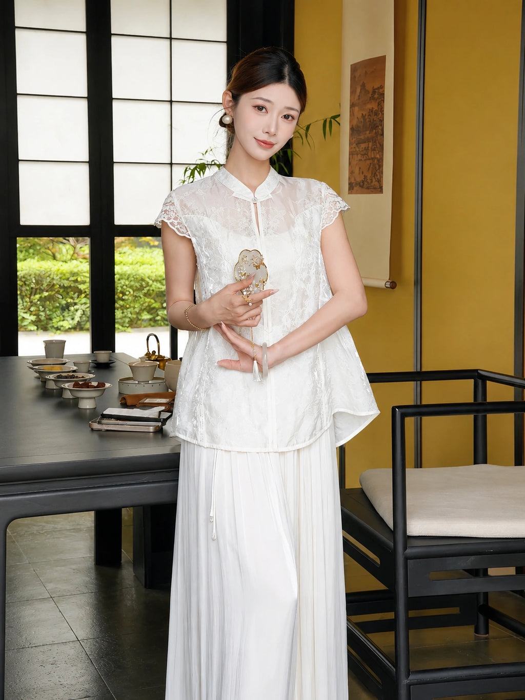 Front view of a white Cheongsam blouse with lace sleeves and embroidery, styled with white pleated pants, holding a fan.