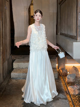 Model wearing a white shiny maxi skirt with a textured top, holding a small handbag, showcasing the elegant drape of the 100% polyester fabric.