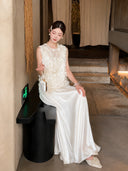 Sitting model in a white shiny maxi skirt, holding a handbag, highlighting the soft, flowy texture of the 100% polyester fabric.