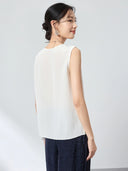 Back view of a white sleeveless V-neck silk blend vest with a relaxed fit and a smooth, flowing drape, paired with dark blue textured pants.