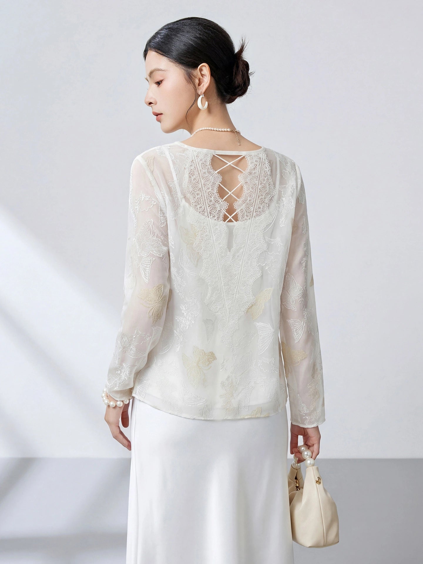 Back view of a white sheer silk top featuring intricate butterfly embroidery, lace panels, and a delicate lace-up criss-cross back detail.