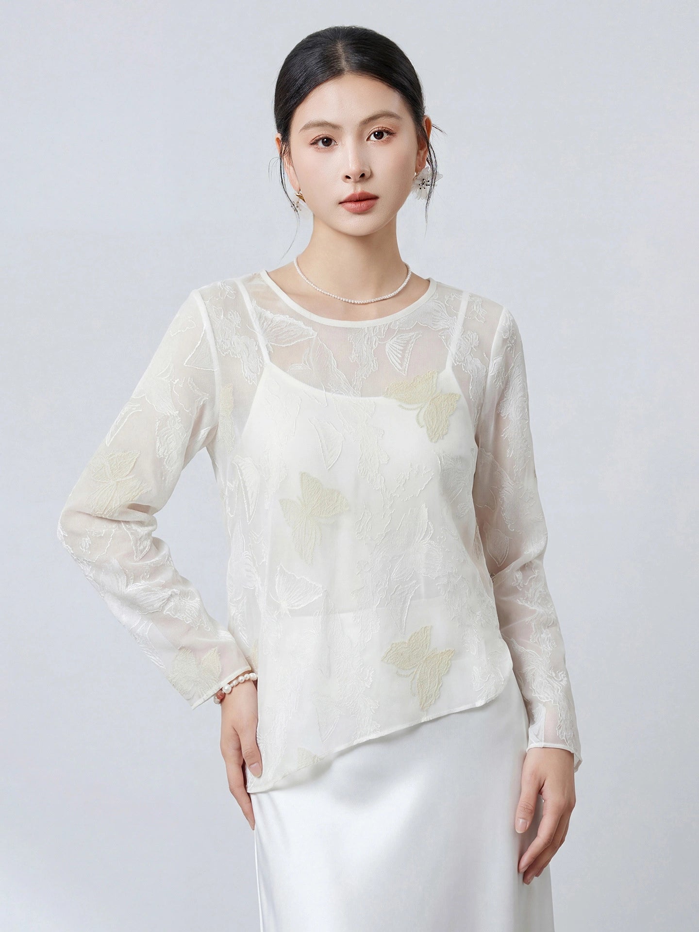Front view of a women's white 100% silk top with a round neckline, sheer fabric, and delicate butterfly embroidery, paired with a white satin skirt.