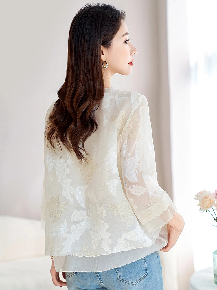 Back view of a model wearing a white silk chiffon cardigan with floral cutwork embroidery, styled with blue jeans, highlighting the airy and delicate design.