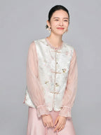 Front close-up of a women's white Tencel vest featuring a round neckline, delicate floral embroidery, and elegant frog buttons, styled with a pink sheer top and satin skirt.