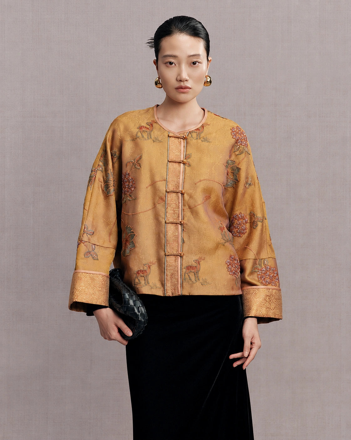 Woman wearing an antique gold floral and deer embroidered silk jacket with a black skirt