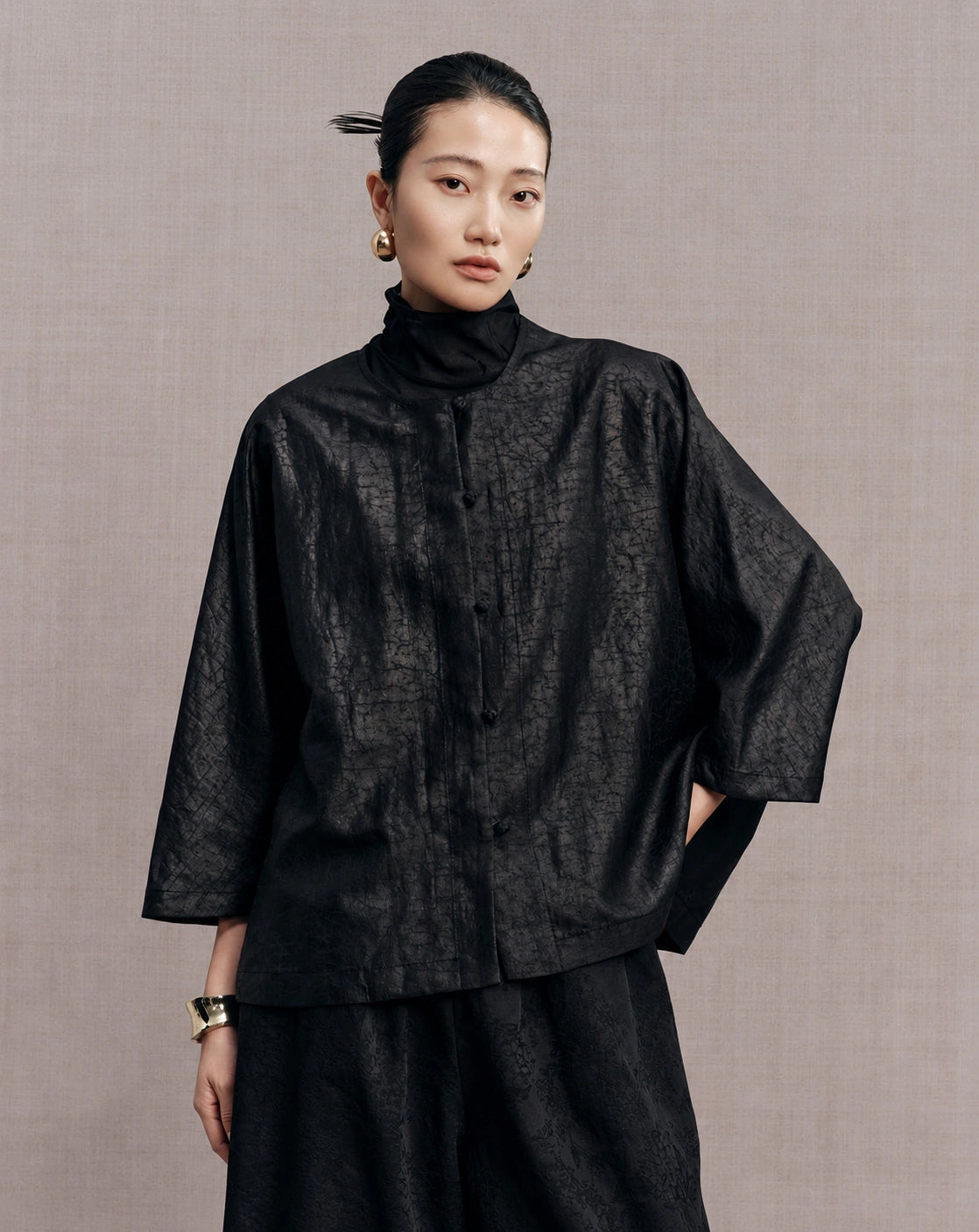 Front detail of the black reversible jacket showing its crackle pattern and button closure