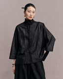 Front detail of the black reversible jacket showing its crackle pattern and button closure