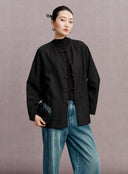 Front view of the loose-fit black jacket showing its round neckline, tonal texture and frog buttons