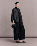 Side view of the black crackle-pattern jacket styled with wide-leg trousers