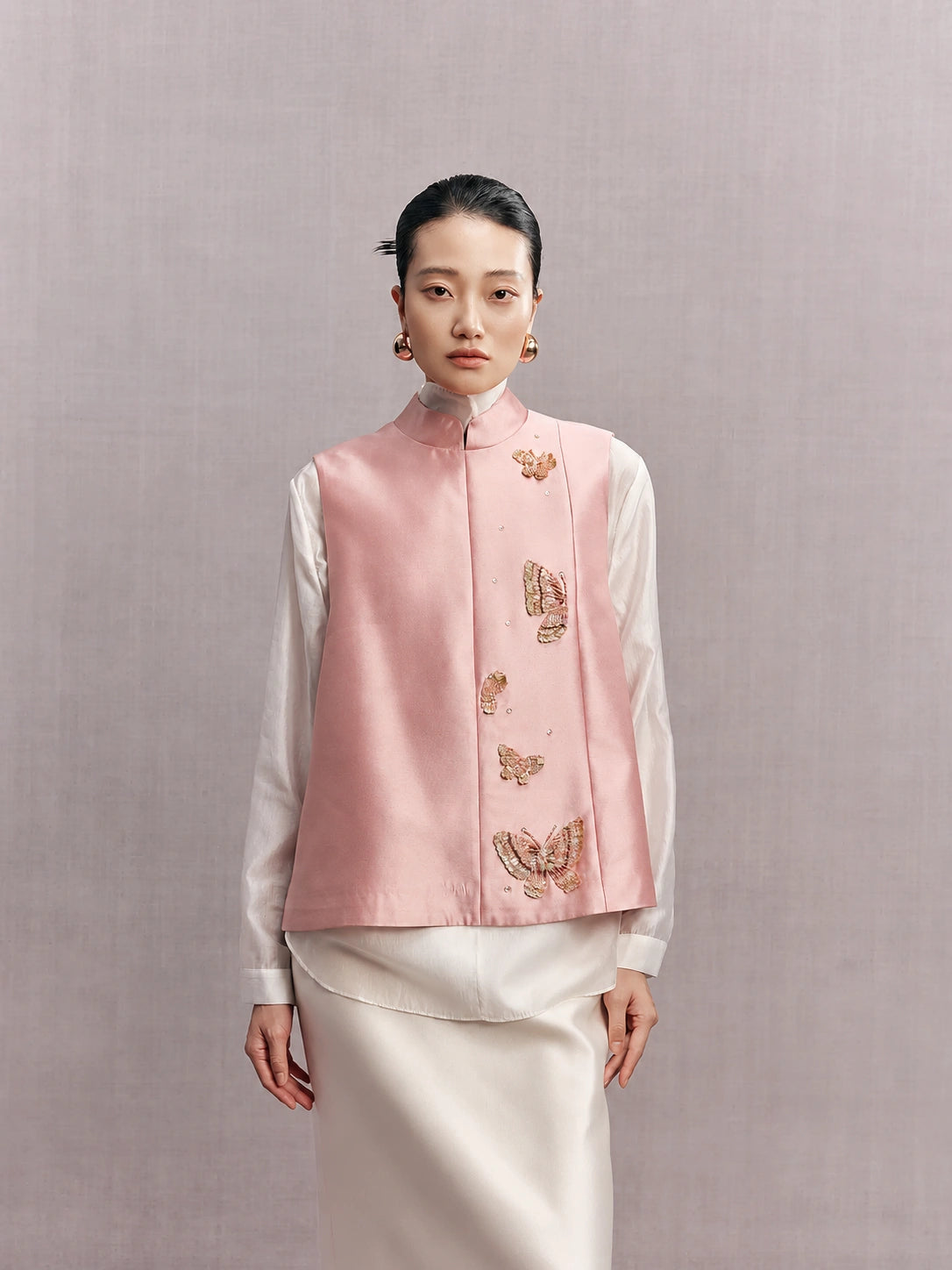 Woman wearing a blush pink silk and wool vest with butterfly embellishments over a white blouse