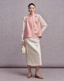 Front view of the blush pink sleeveless New Chinese vest styled with an ivory skirt