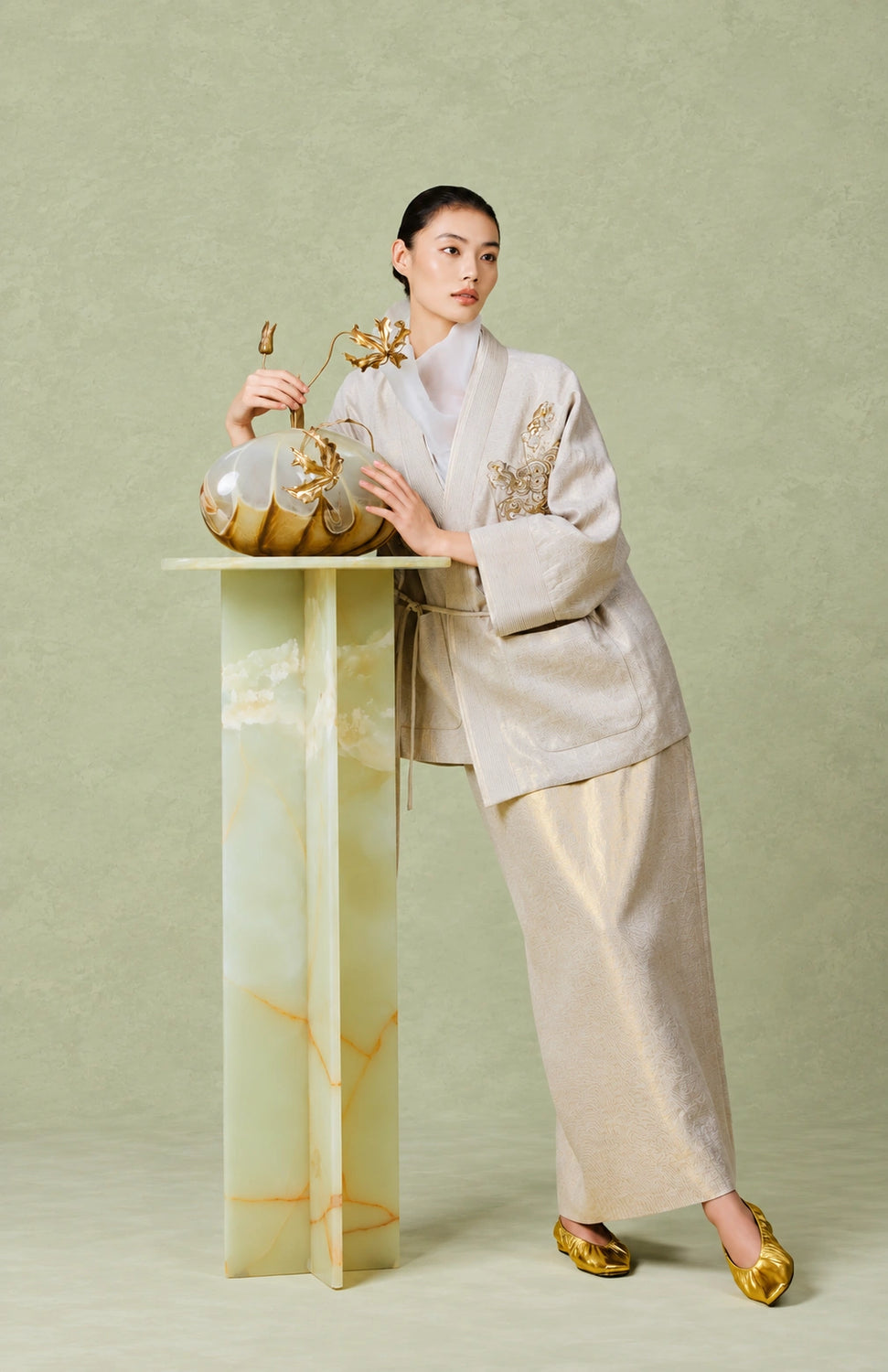 Woman wearing the champagne beige embroidered jacket and matching long skirt beside a decorative vase