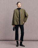 Olive green New Chinese jacket worn open over a black top with cropped trousers