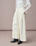Angled view of white high-waisted jacquard wide-leg pants showing the floral pattern and side pocket