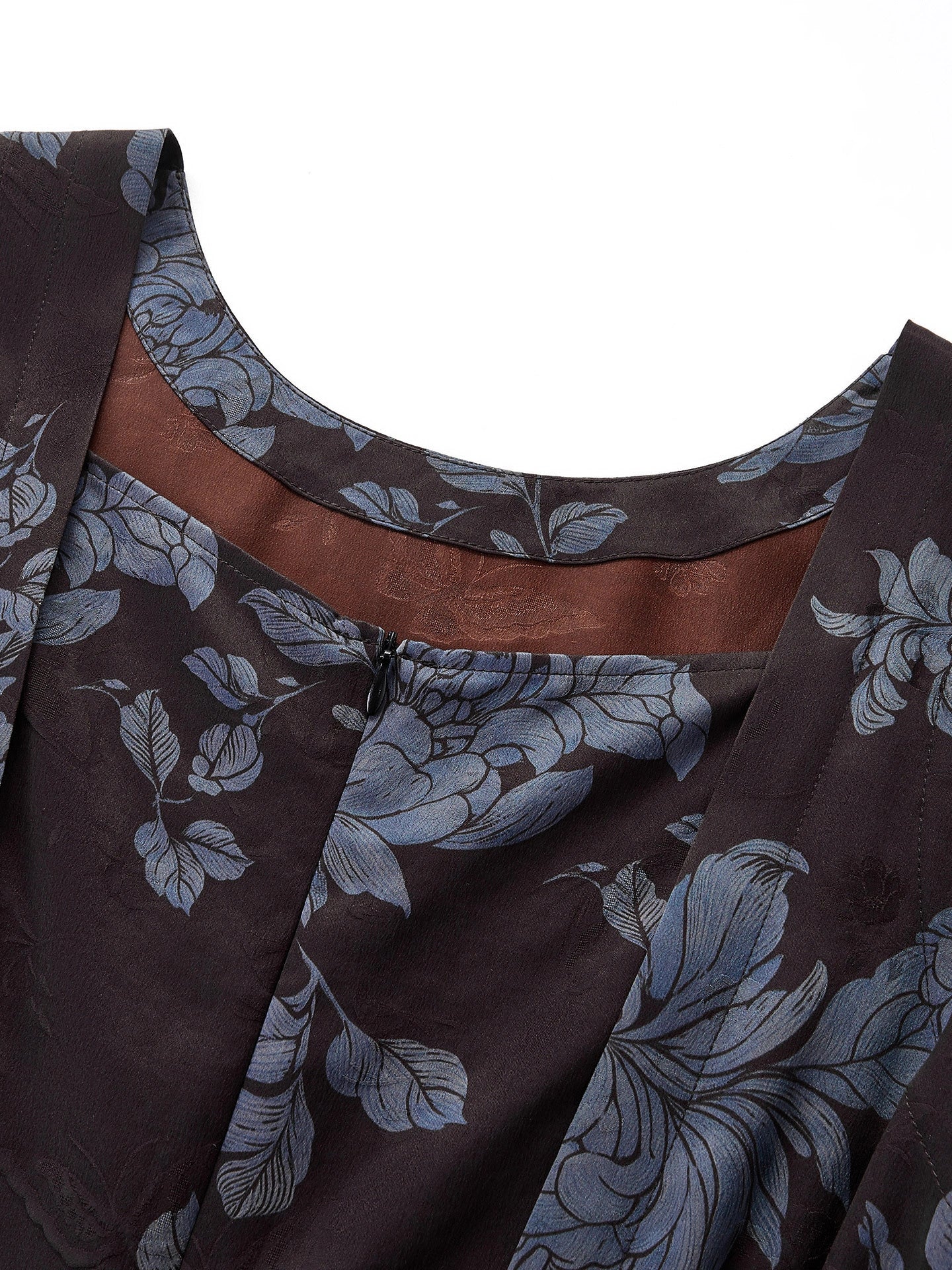 Close-up of the round neckline and back zipper of a brown Xiangyunsha silk dress, highlighting the intricate blue floral jacquard texture and the contrast brown lining.