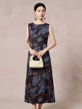 Model wearing a dark brown 100% mulberry silk sleeveless dress with a round neckline and blue floral jacquard pattern, holding a cream handbag.