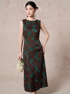 Front view of a dark brown mulberry silk dress with a round neckline, sleeveless design, and elegant green floral jacquard pattern, styled with a cream handbag.