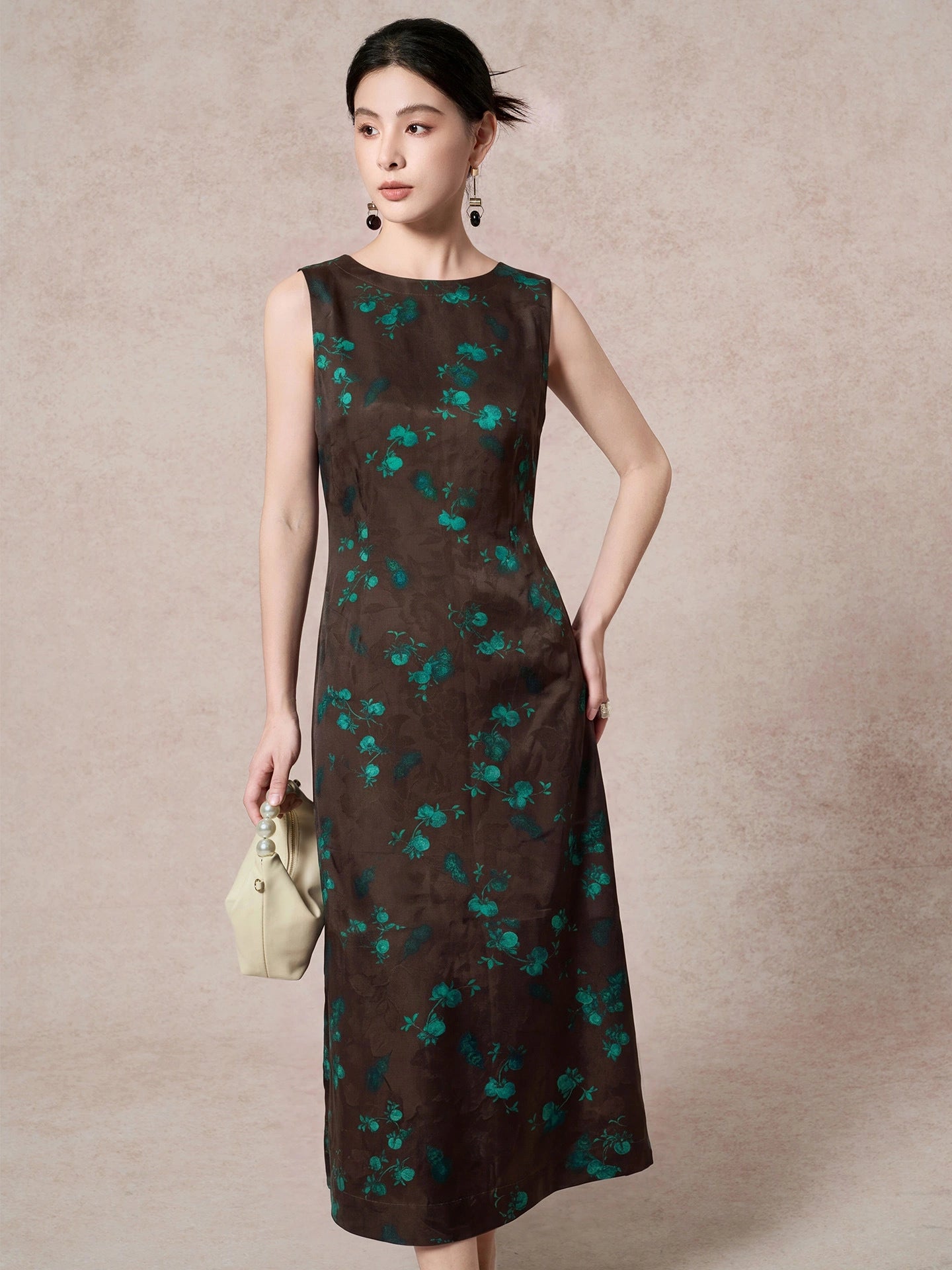Front view of a dark brown mulberry silk dress with a round neckline, sleeveless design, and elegant green floral jacquard pattern, styled with a cream handbag.