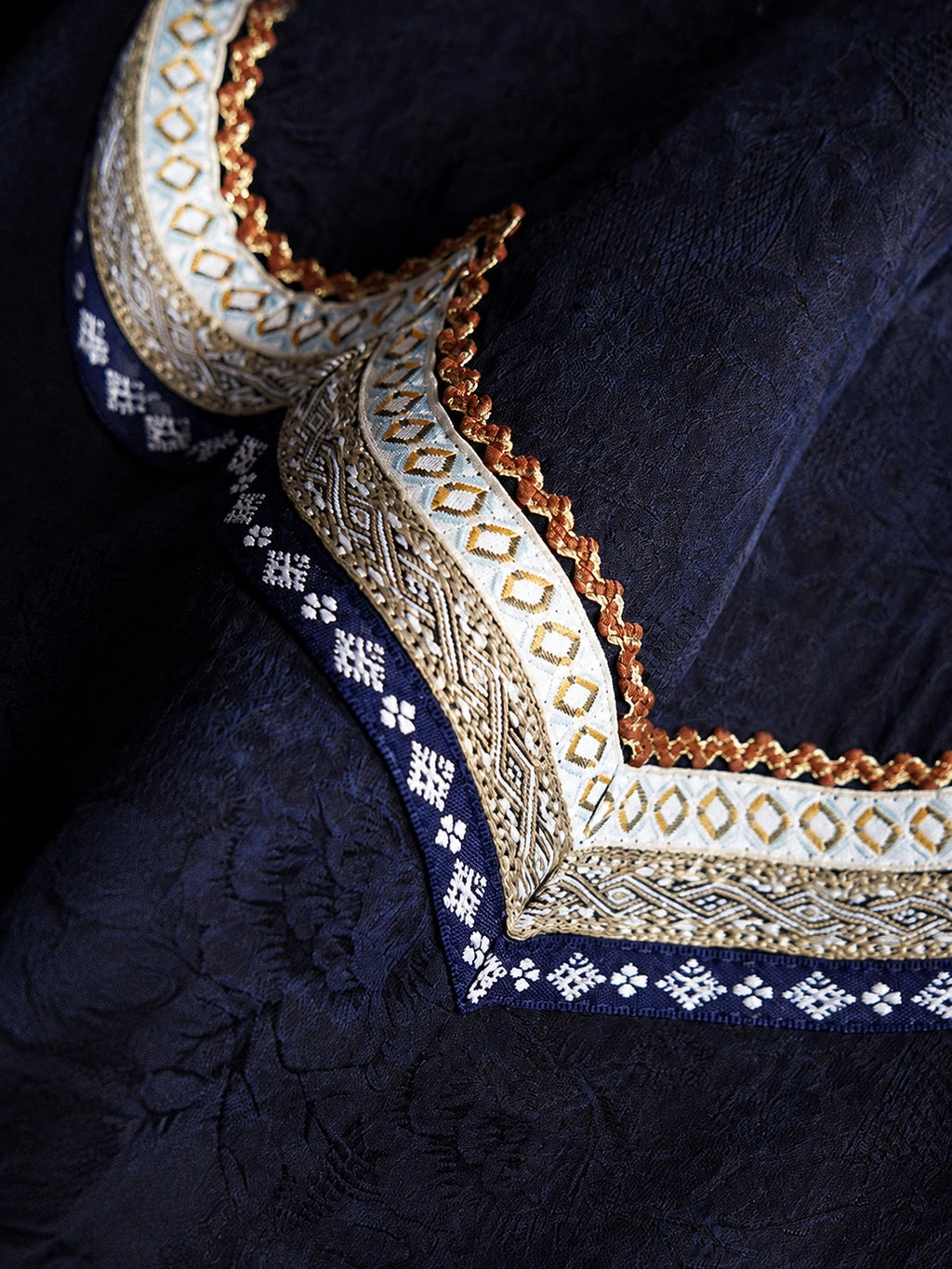 Close-up of the layered geometric neckline embroidery on midnight navy Xiangyunsha silk fabric