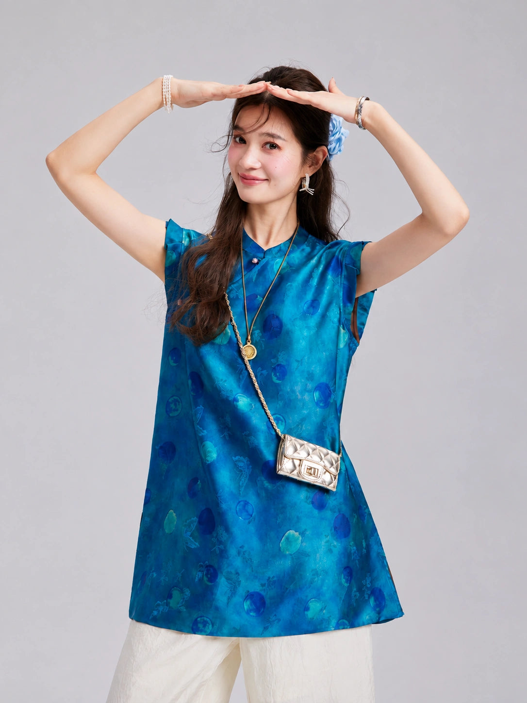 Woman styling a mid-length blue Xiangyunsha sleeveless top with white trousers