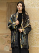 Three-quarter view of the Xuye jacket showing black leather sleeves, patterned cashmere cuffs, and fringed shawl panels