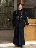 Model wearing the Yanchuan black jacket with dark wide-leg trousers and black boots beside a wooden window.