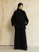 Model looking down while wearing Yangui black wide-leg pants beneath a relaxed black jacket.