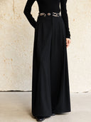 Closer view of Yangui black pants highlighting the embroidered velvet waistband, front pleats and wide-leg silhouette.