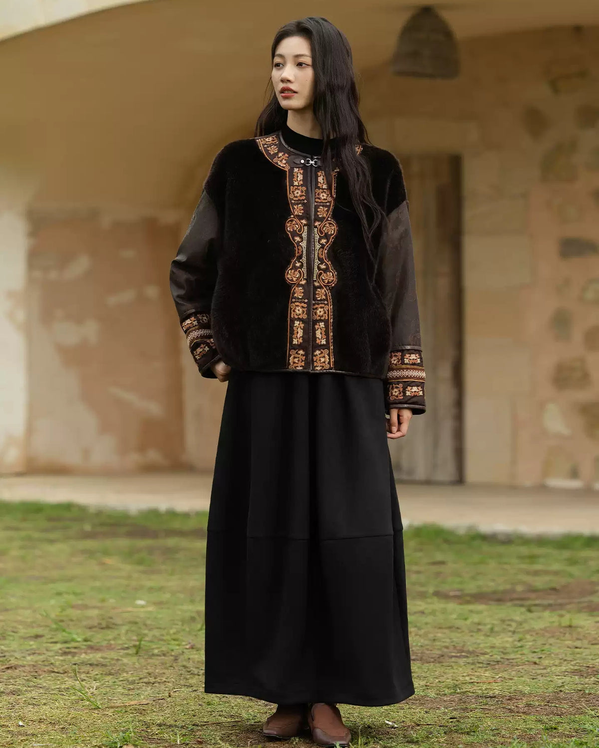 Black silk and shearling jacket with embroidered borders, paired with flowing black wide-leg trousers
