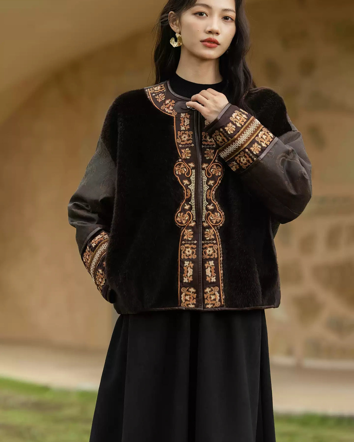 Close view of the jacket showing its embroidered neckline and cuffs, metal clasp, and contrasting silk and shearling textures