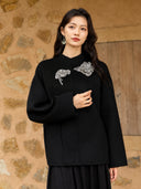Front detail of the black wool coat showing its round neckline, silver-tone floral embroidery, and wide sleeves