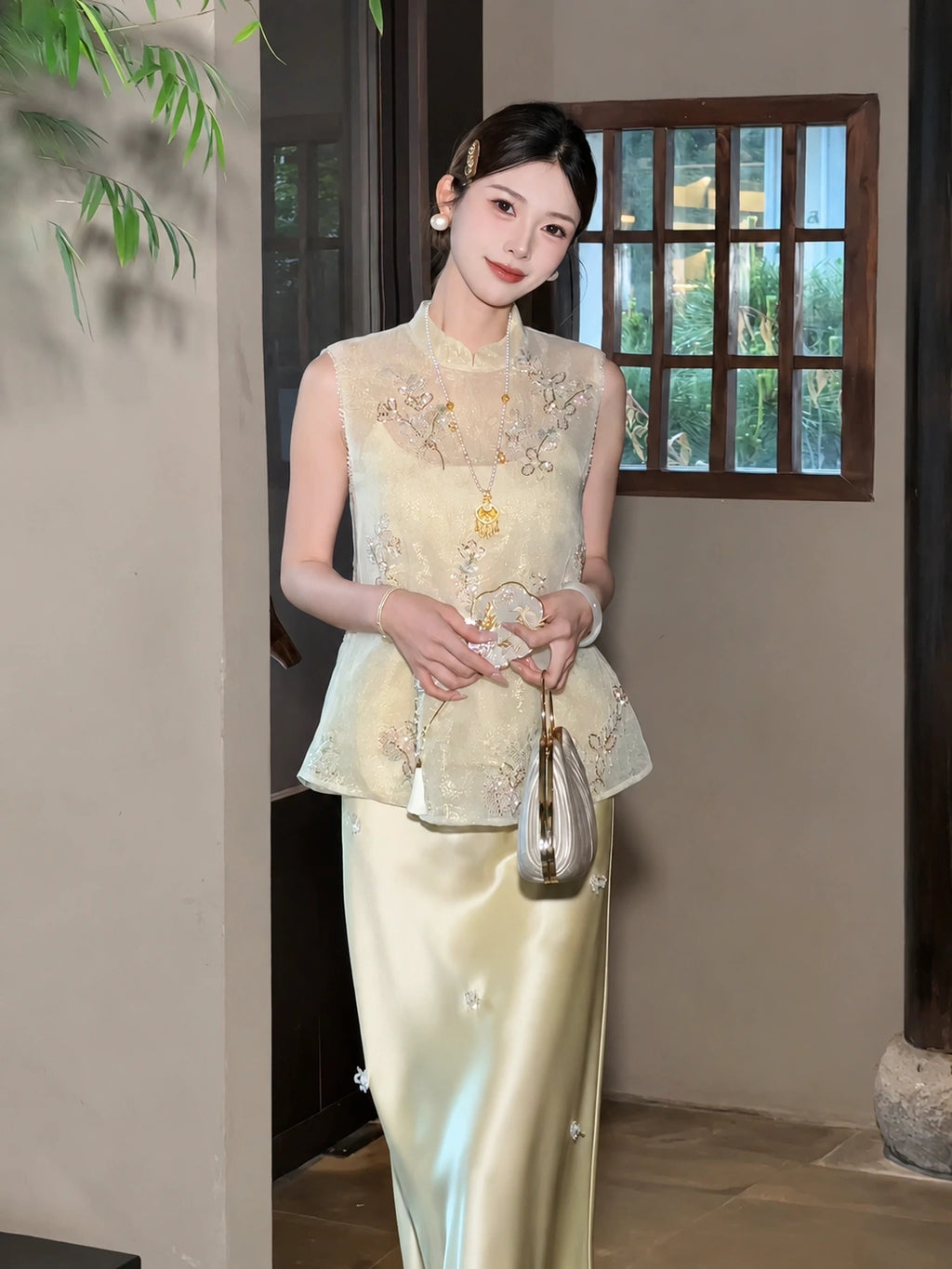 Model wearing a yellow beaded Cheongsam vest with a mandarin collar and floral embroidery, holding a fan, styled with a yellow satin skirt.