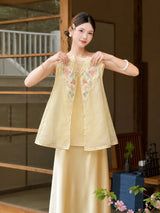 Model wearing a yellow sleeveless Cheongsam vest with intricate floral embroidery and a matching satin skirt, adjusting the collar, crafted from 100% polyester.