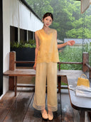 Model in a yellow Cheongsam vest and matching pants, holding a clear umbrella and a yellow handbag on a rainy day, crafted from 73% Viscose and 27% Polyester.