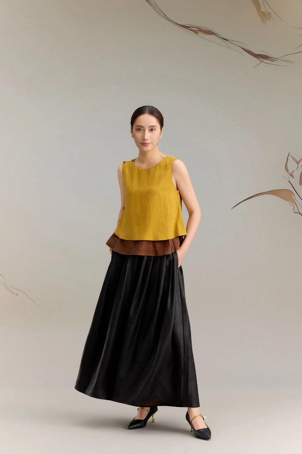 Front view of a yellow silk sleeveless blouse with a round neckline and layered brown underlay, styled with black wide-leg pants, featuring 100% silk fabric.