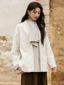 Front detail of the ivory coat showing botanical jacquard, an asymmetrically draped wool-blend panel, and a gold-tone accent