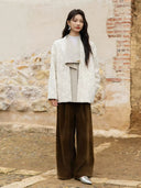 Full-length view of the Yongyan ivory botanical jacquard coat with a draped front panel, styled with brown wide-leg trousers