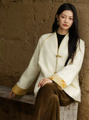 Model seated on a wooden bench wearing the Yuanting ivory jacquard jacket with gold-tone piping and patterned cuffs.