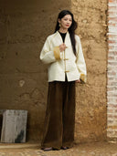 Model wearing the Yuanting ivory jacket with brown wide-leg trousers beside a textured wall.