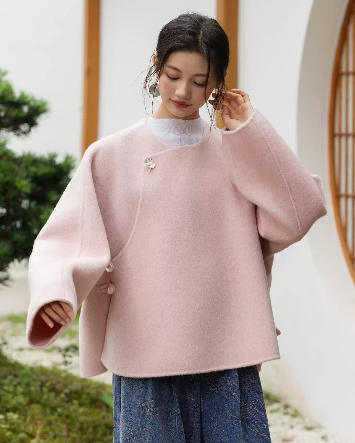 Blush pink Yuyan wool coat with a round neckline, asymmetric overlapping front, and curved hem