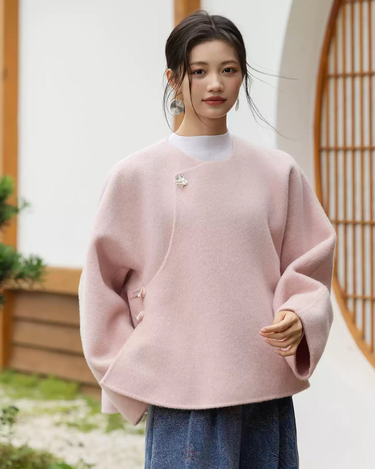 Front view of the blush pink wool coat showing side button details, wide sleeves, and a rounded hem